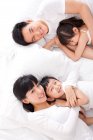 Feliz familia china acostada en la cama - foto de stock
