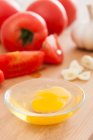 Ingredientes para cocinar sobre tabla de madera, ajo, huevo en tazón y tomates - foto de stock