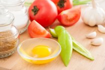 Ingredientes para cocinar sobre tabla de madera, ajo, huevo en tazón y tomates - foto de stock