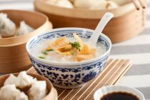 Bowl of rice porridge with crisps and chopped green onion with spoon — Stock Photo