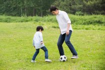 Happy Chinese father and son playing football together — Stock Photo