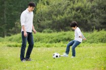 Feliz padre chino e hijo jugando fútbol juntos - foto de stock