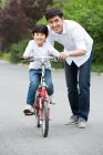 Padre chino enseñando a su hijo a montar en bicicleta - foto de stock