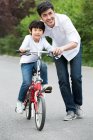 Chinese father teaching son to ride a bicycle — Stock Photo