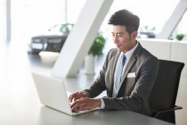 Young chinese businessman working with laptop in office — Stock Photo