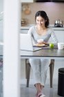 Young Chinese woman using laptop while having breakfast — Stock Photo