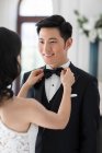 Joven esposa china ajustando corbata de lazo para su marido - foto de stock