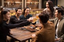 Happy Chinese friends toasting and talking in bar — Stock Photo