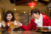 Young Chinese couple drinking beer in hotpot restaurant — Stock Photo