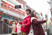 Jovem casal chinês tomando auto retrato com telefones inteligentes — Fotografia de Stock