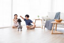 Feliz irmão chinês brincando com o cão na sala de estar — Fotografia de Stock