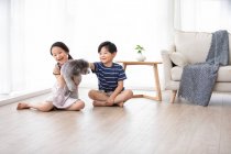 Happy Chinese sibling playing with dog in living room — Stock Photo