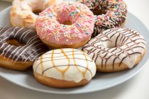 Delicious donuts on plate with various glaze and sprinkles — Stock Photo