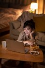 Женщина смотрит кино на ноутбуке и берет закуски из миски — стоковое фото