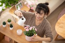 Giovane donna cinese che innaffia fiori a casa — Foto stock