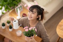 Jeune femme chinoise arrosant des fleurs à la maison — Photo de stock