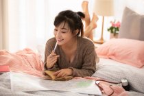 Woman making travel plan at home, lying on bed with map — Stock Photo