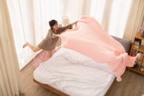 Young Chinese woman making bed at home — Stock Photo