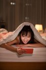 Junge Chinesin mit Smartphone im Bett — Stockfoto
