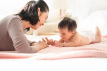 Giovane mamma cinese sorridente e giocando con il bambino sul divano — Foto stock
