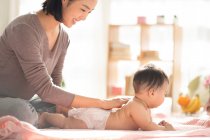 Young chinese mom smiling and playing with baby on couch — Stock Photo