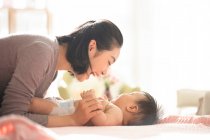 Joven madre china sonriendo y jugando con el bebé en el sofá - foto de stock
