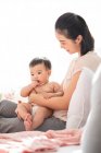 Joven madre china sosteniendo a su bebé mientras está sentada en el sofá - foto de stock
