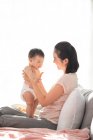 Jovem chinesa mãe segurando seu bebê enquanto sentado no sofá — Fotografia de Stock