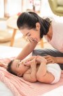 Jeune maman chinoise souriant et jouant avec bébé sur le canapé — Photo de stock
