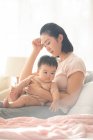 Stanco mamma holding bambino mentre seduto su divano con mano dalla testa — Foto stock