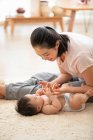 Jeune mère jouer avec bébé couché sur le tapis — Photo de stock
