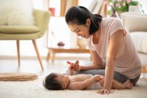 Giovane madre che gioca con il bambino sdraiato su tappeto — Foto stock