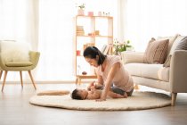 Молода мати грає з дитиною, лежачи на килимі — стокове фото
