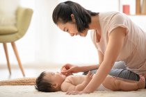 Giovane madre che gioca con il bambino sdraiato su tappeto — Foto stock