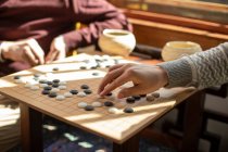 Cropped shot of senior man hand playing game of go, other man on background — Stock Photo