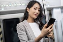 Junge chinesische Geschäftsfrau benutzt Smartphone in U-Bahn — Stockfoto