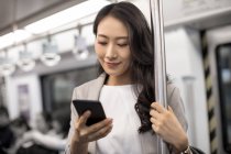 Junge chinesische Geschäftsfrau benutzt Smartphone in U-Bahn — Stockfoto