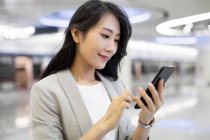 Молодая китаянка пользуется смартфоном в аэропорту — стоковое фото