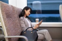 Woman sitting in high-speed train with coffee cup and using smartphone — Stock Photo
