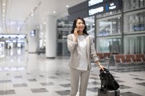 Женщина с багажом разговаривает по телефону в аэропорту — стоковое фото