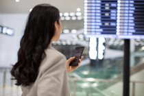 Junge Chinesin benutzt Smartphone am Flughafen — Stockfoto