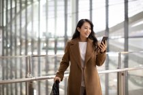 Женщина со смартфоном и багажом в аэропорту — стоковое фото