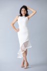 Schöne asiatische Frau posiert in weißem Kleid auf grauem Studiohintergrund — Stockfoto