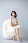 Schöne Chinesin posiert auf flauschigem Sessel in weißem Kleid und High Heels — Stockfoto
