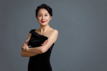 Beautiful mature chinese woman posing in black dress on gray studio background — Stock Photo
