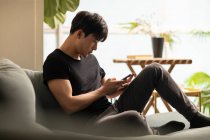 Young chinese man using smartphone while sitting on couch — Stock Photo