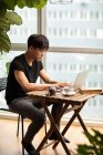 Young chinese man using laptop at table with book, coffee cup and vintage camera — Stock Photo
