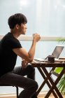 Молодий китайський чоловік сидить з чашкою кави за столом з ноутбуком — стокове фото
