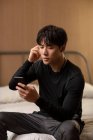 Молодий китайський чоловік дивиться на екран смартфона і використовує навушники — стокове фото