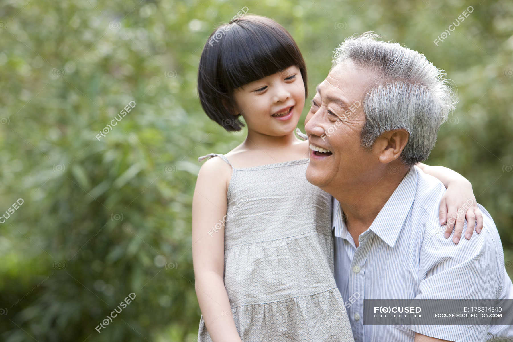 Chinese Grandpa And Granddaughter Embracing And Laughing In Garden